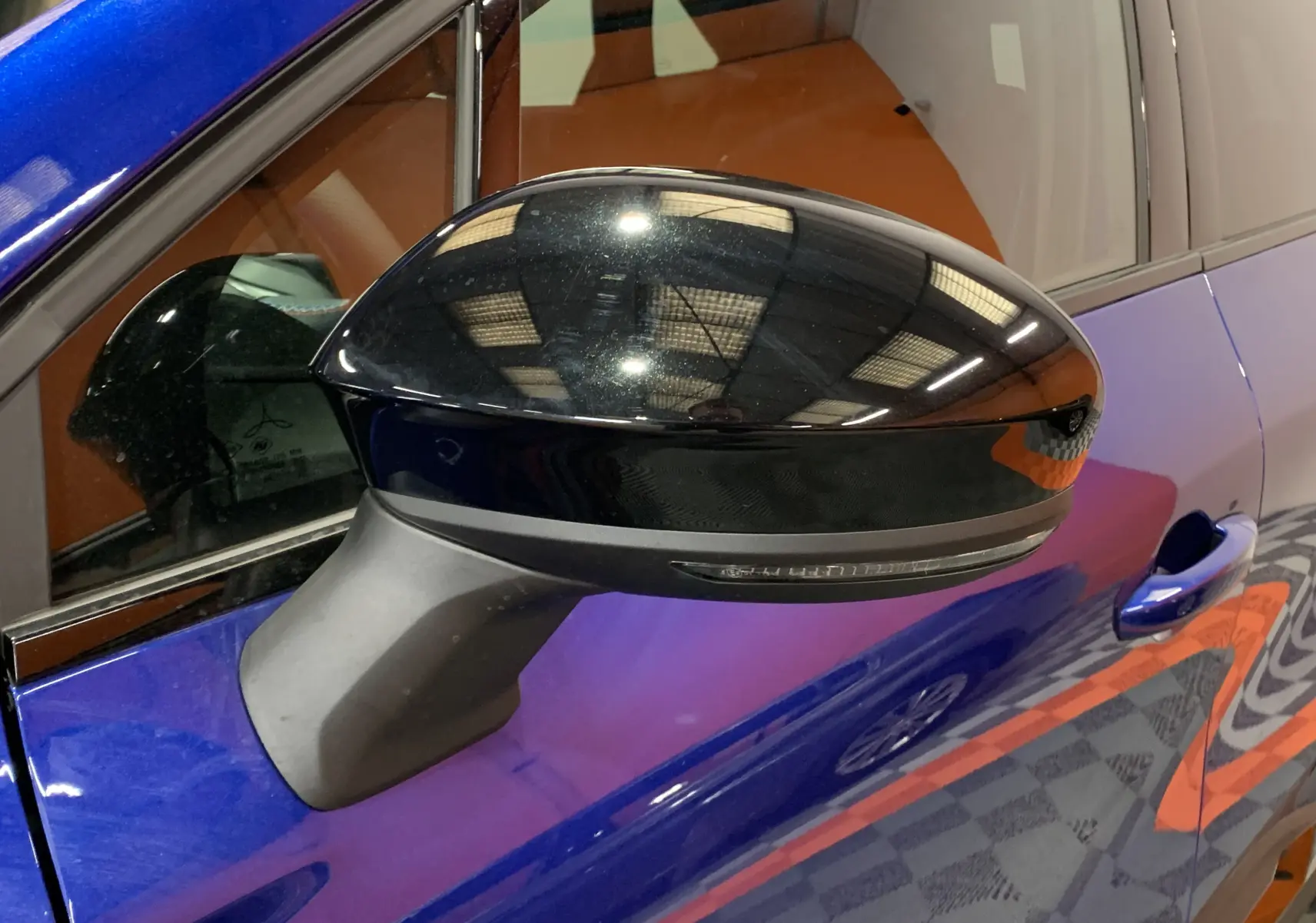 Rétroviseur noir brillant côté gauche sur Renault Symbioz bleu iron, avec reflet de l’éclairage intérieur visible.