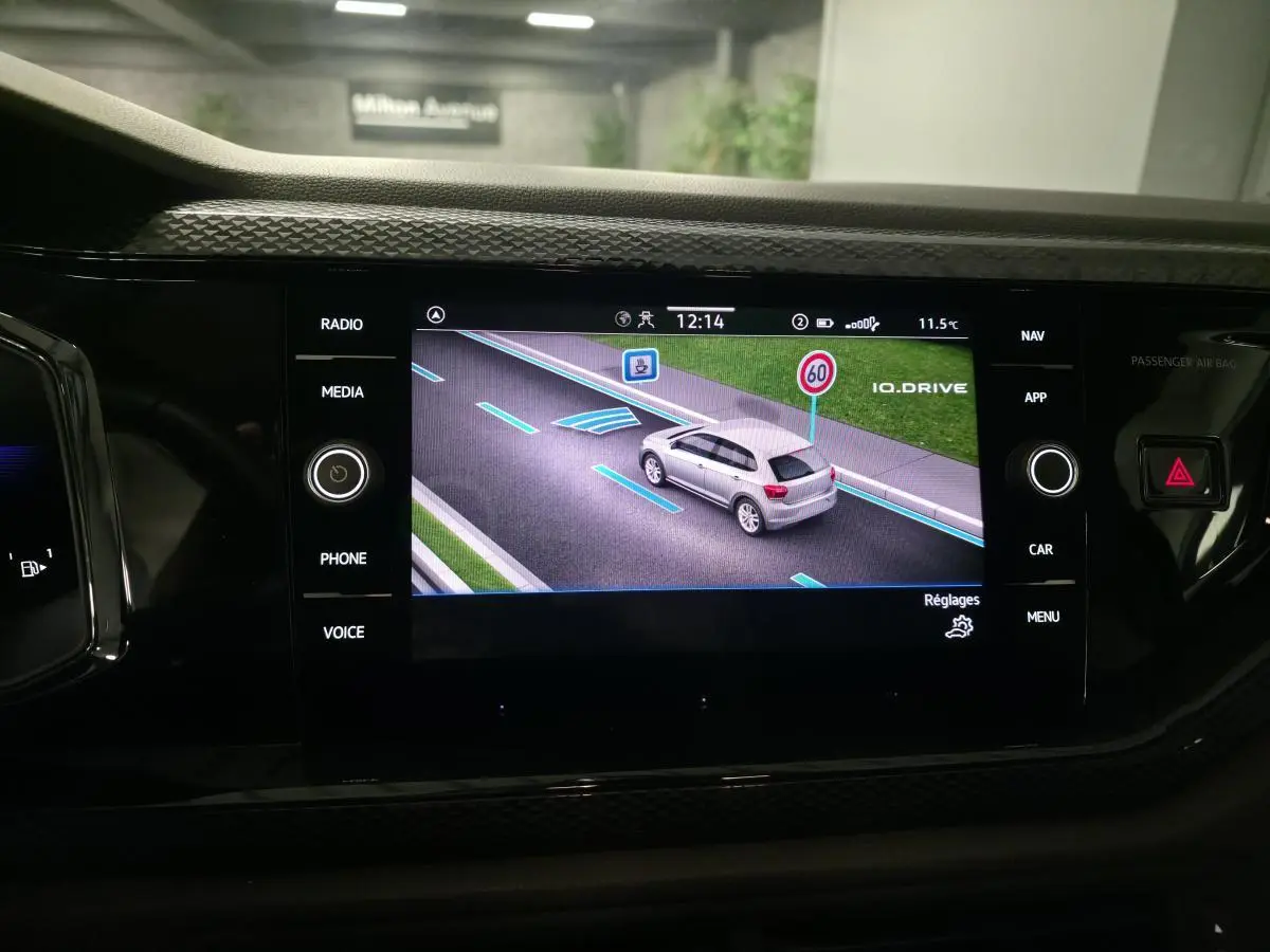 Écran tactile intérieur affichant la vue 3D d'une Volkswagen Polo grise en circulation avec indication de limitation de vitesse.