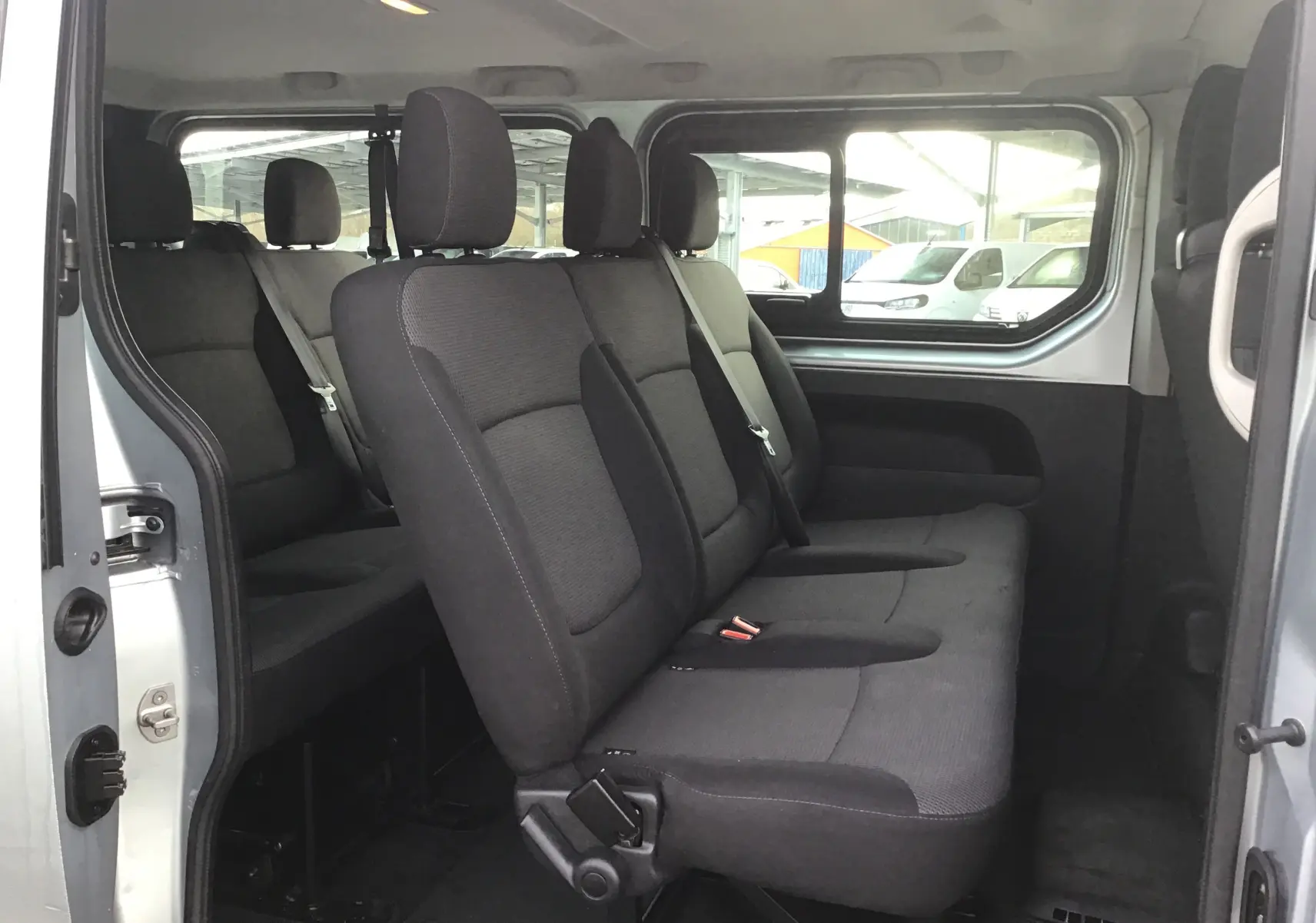 Vue intérieure côté droit sur les sièges noirs du Renault Trafic Combi gris clair métal, version 9 places, porte latérale ouverte.
