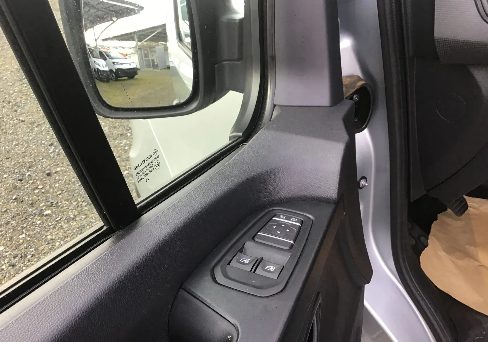 Gros plan sur la commande des vitres et rétroviseurs côté conducteur d’un Renault Trafic Combi gris clair 2023.