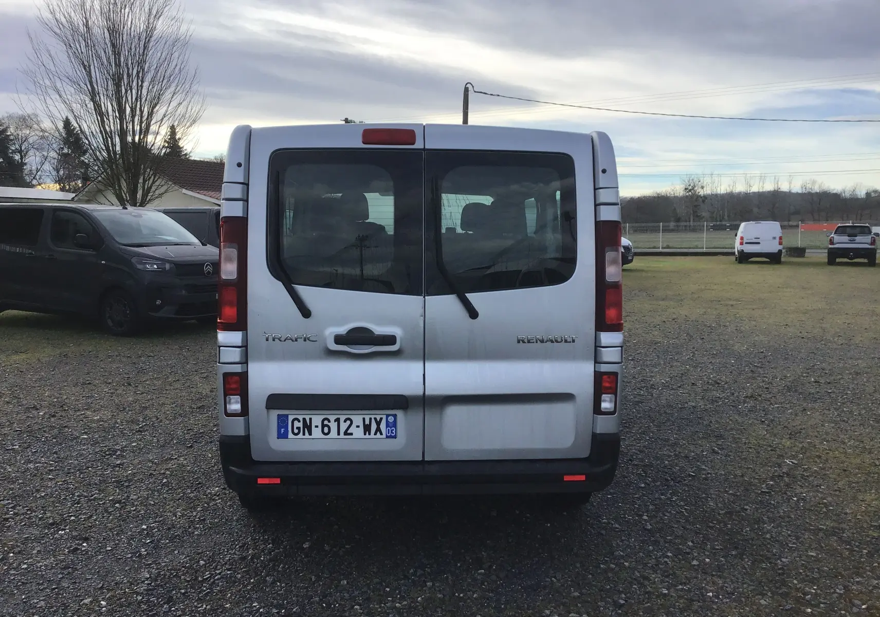Vue arrière d’un Renault Trafic Combi gris clair métal, avec portes vitrées et essuie-glaces arrière visibles.