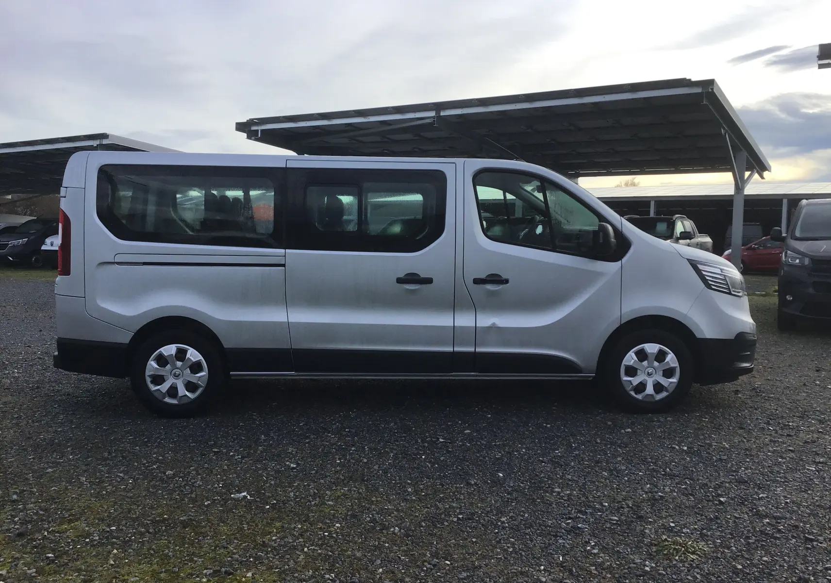 Profil côté gauche d'un Renault Trafic Combi gris clair métal 2023, véhicule utilitaire spacieux avec vitres teintées.