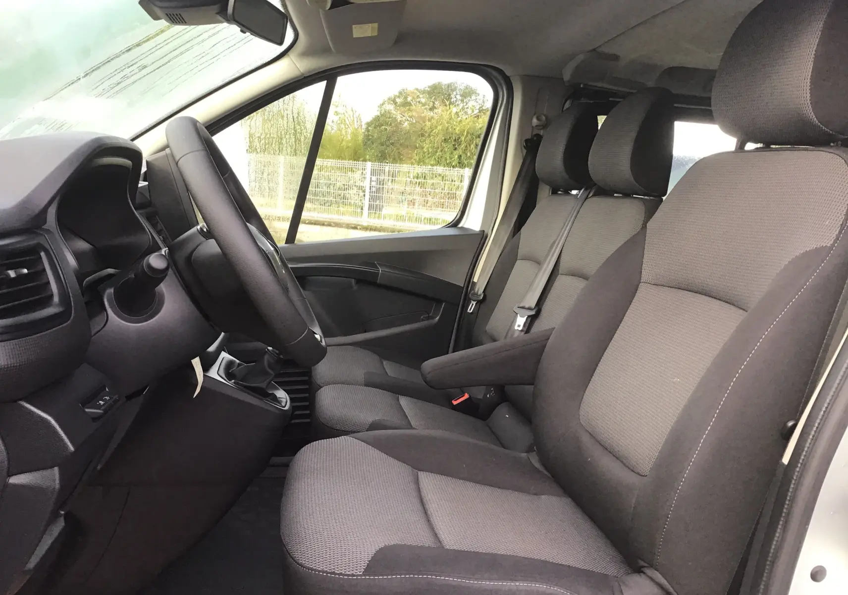 Vue intérieure côté conducteur du Renault Trafic Combi gris clair 2023, montrant les sièges avant et le volant.