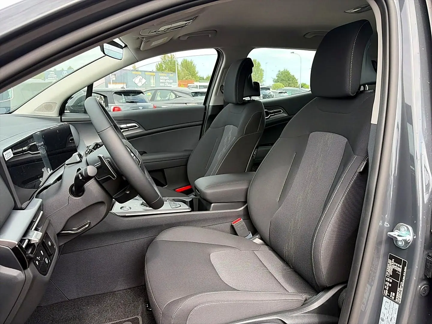 Vue intérieure côté conducteur du Kia Sportage gris eclipse 2026, avec sièges tissu et volant multifonction cuir.
