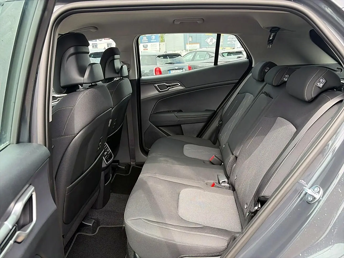 Vue intérieure côté droit des sièges arrière gris du Kia Sportage 1.6 hybride 239 active avec appuie-têtes et ceintures visibles.