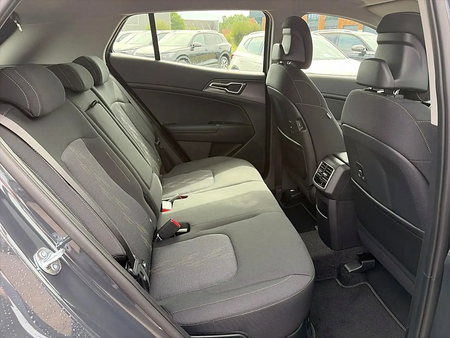 Vue intérieure côté droit montrant la banquette arrière grise du Kia Sportage 1.6 hybride 239 active 2026 avec appuie-têtes et aérateurs centraux.