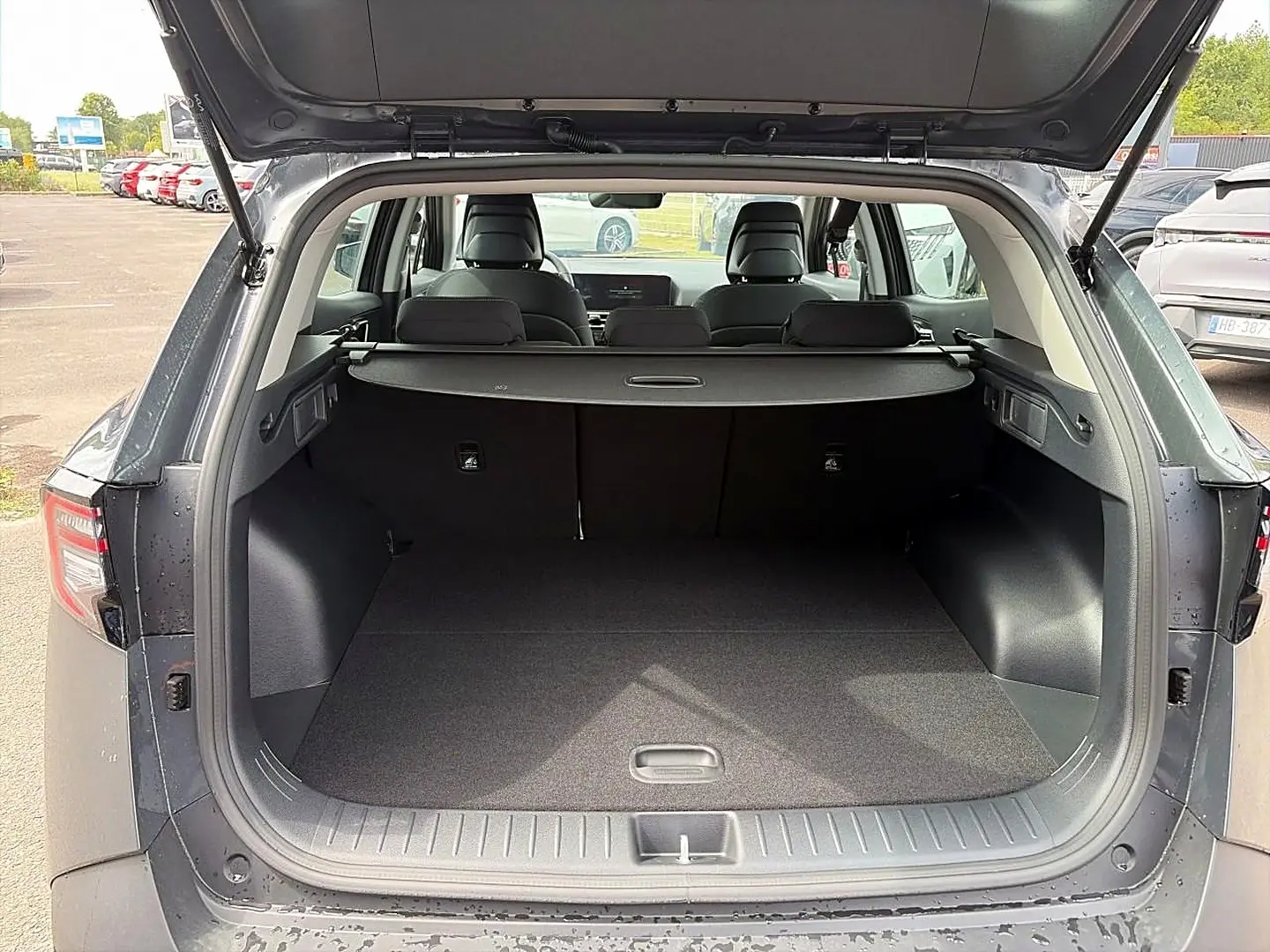 Coffre ouvert vu de l’arrière d’un KIA Sportage gris eclipse 2026 avec cache-bagages et banquette rabattue.