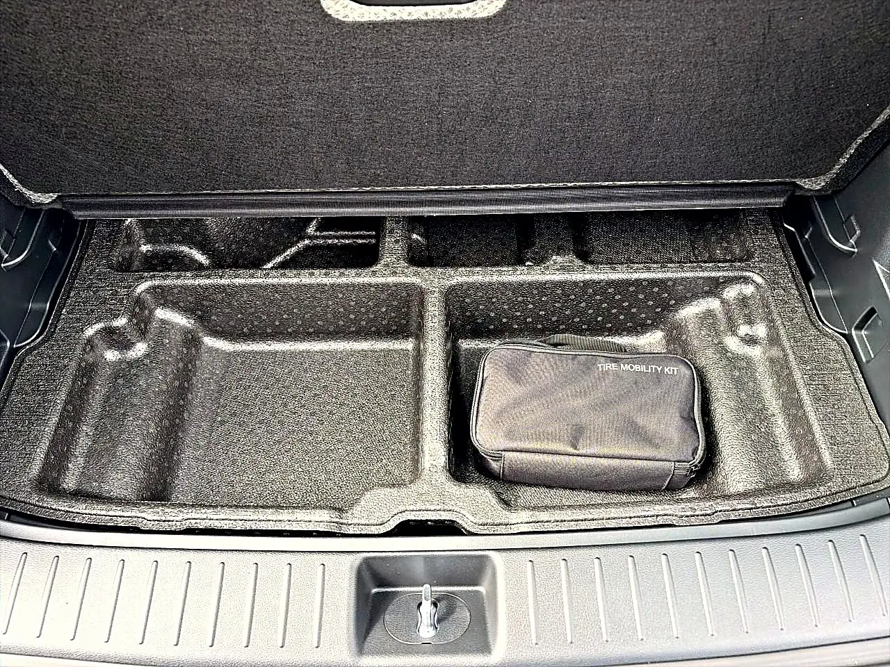 Coffre ouvert du Kia Sportage gris eclipse 2026 montrant le rangement sous plancher avec kit mobilité pneus.
