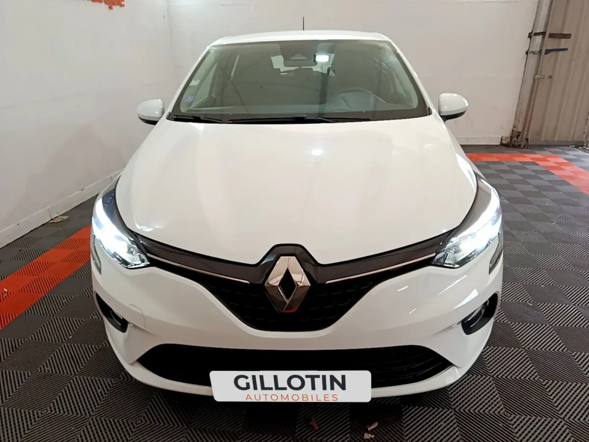 Vue avant d'une Renault Clio Business blanche avec phares LED allumés dans un garage intérieur.