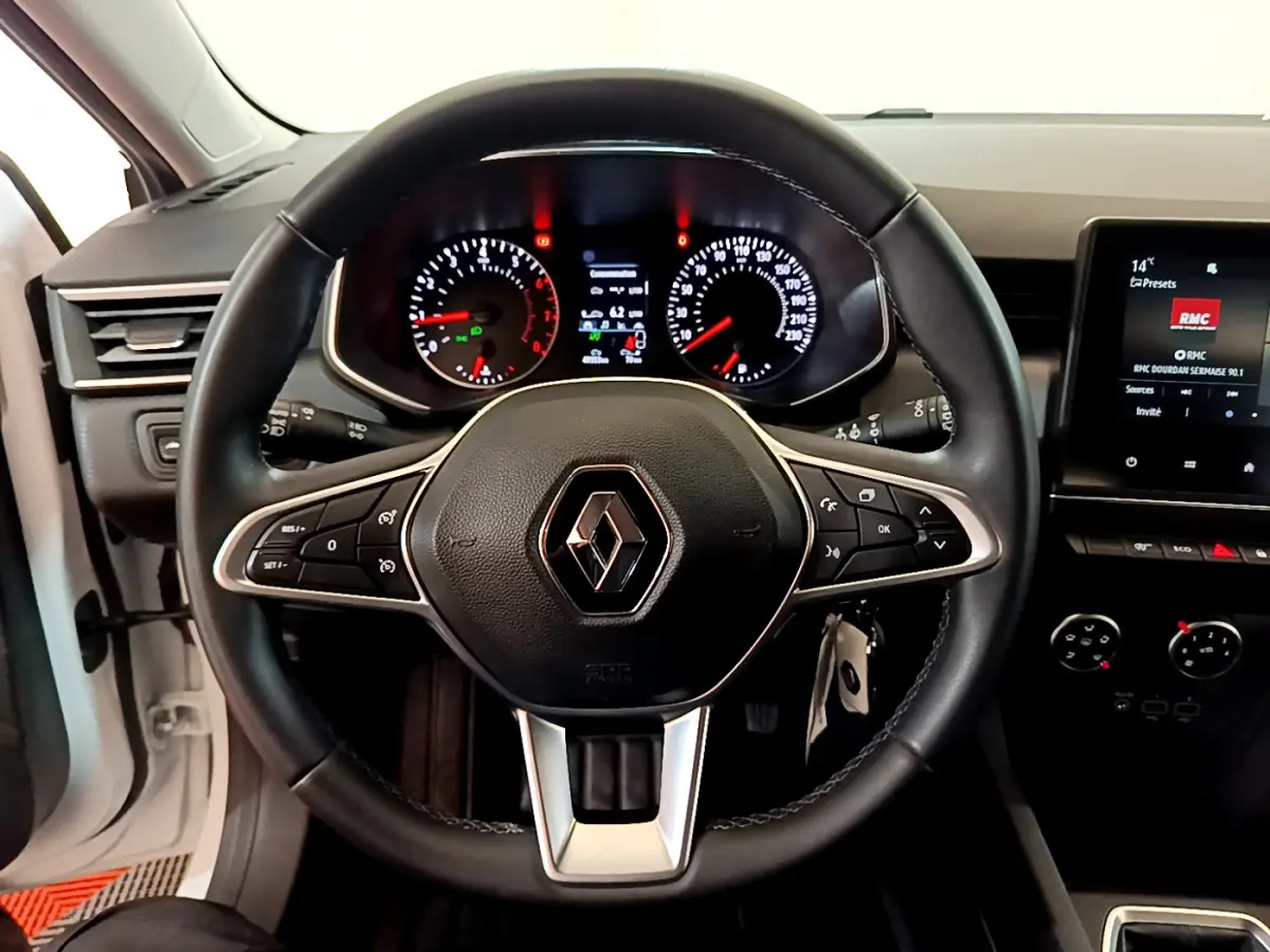 Vue intérieure centrée sur le volant cuir noir de la Renault Clio Business blanc, avec tableau de bord et écran tactile visibles.