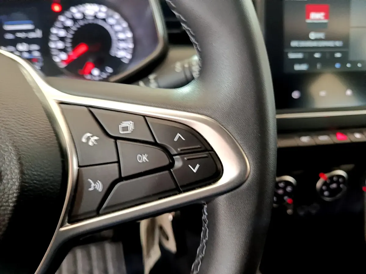 Gros plan sur les commandes du volant côté gauche d'une Renault Clio Business blanche de 2021, tableau de bord flou en arrière-plan.