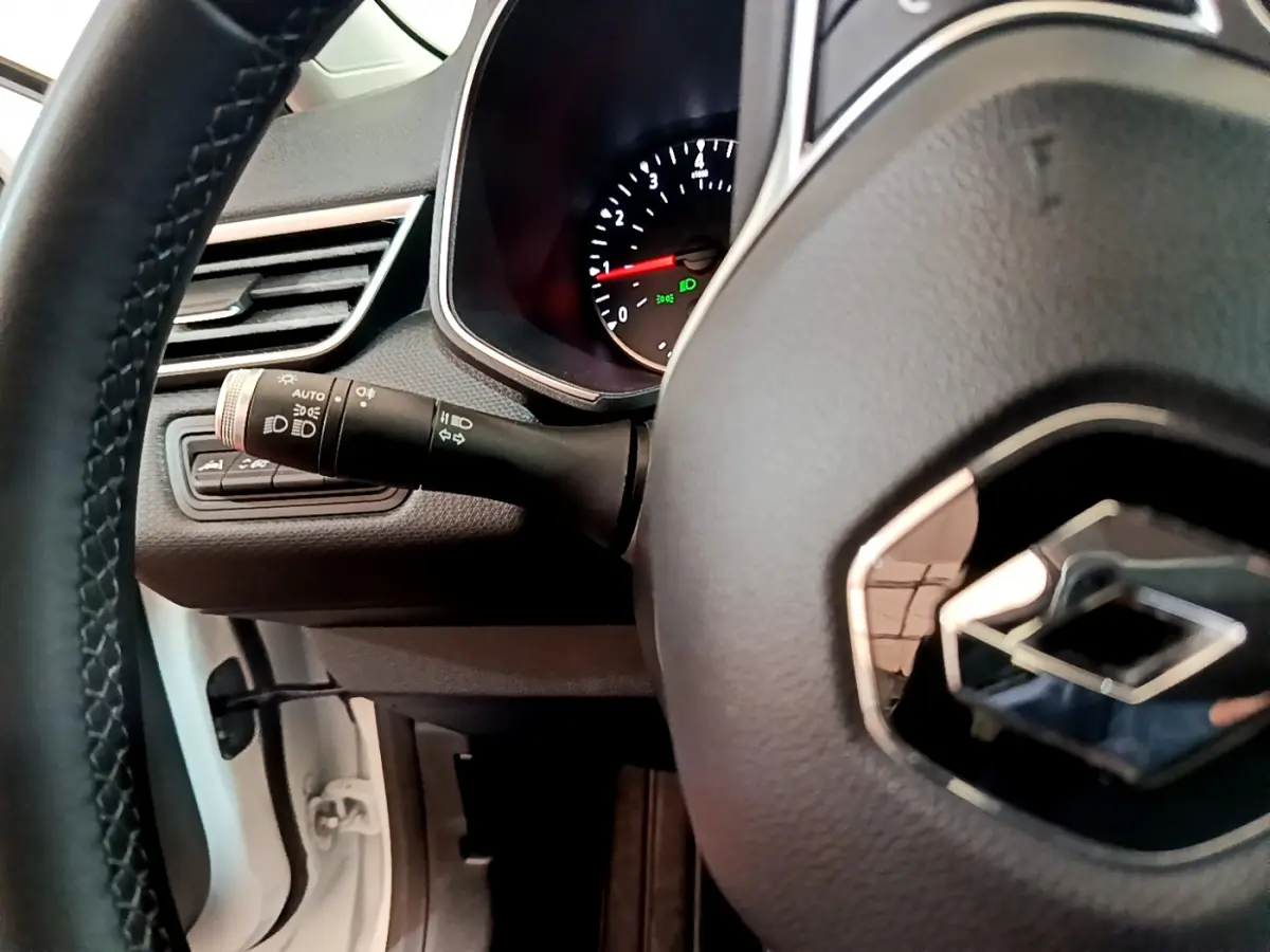 Vue rapprochée du volant cuir et du tableau de bord d'une Renault Clio Business blanche, avec commandes lumineuses visibles.