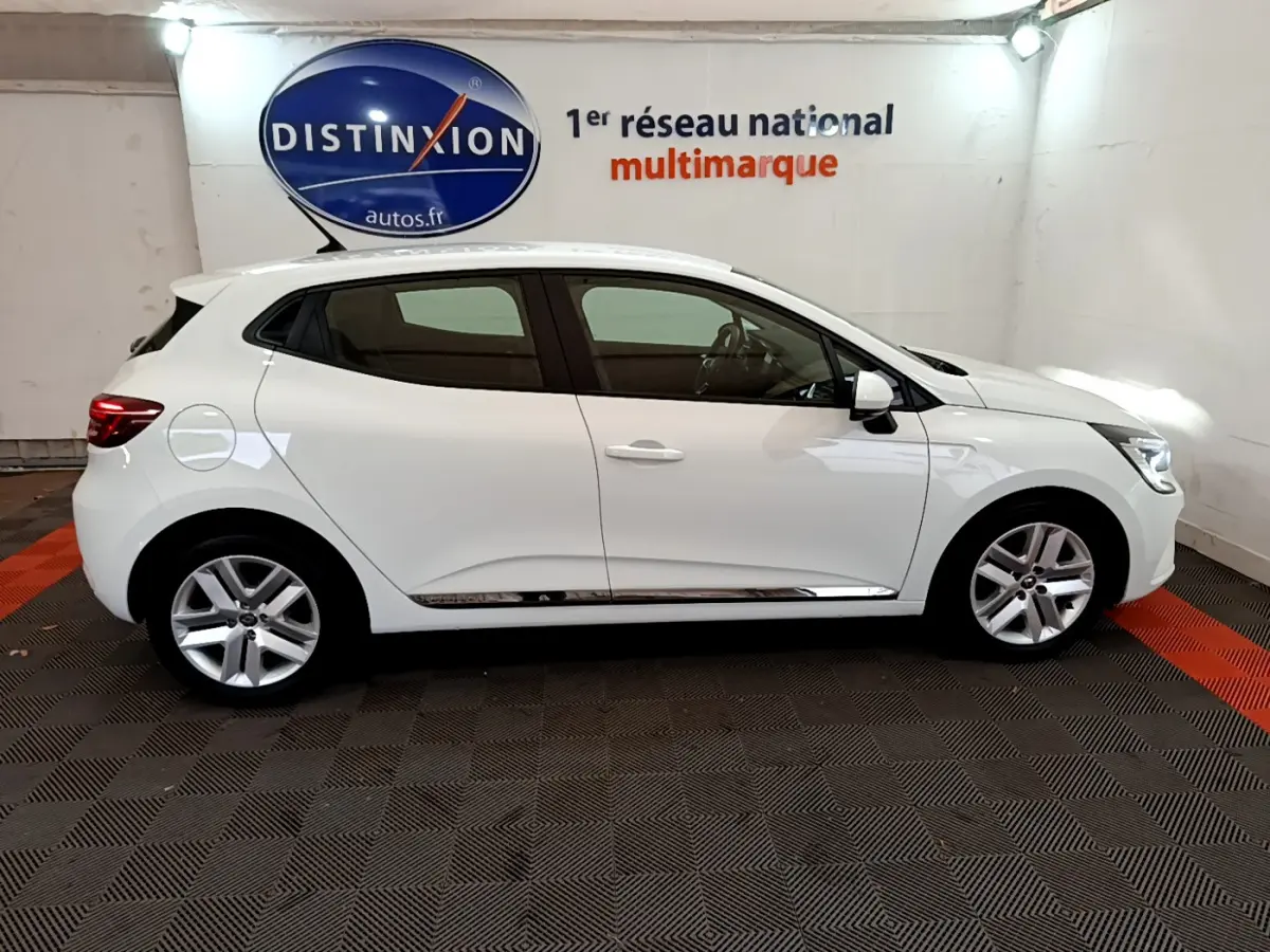Profil droit d'une Renault Clio Business blanche 2021 dans un showroom avec logo Distinxion en arrière-plan.