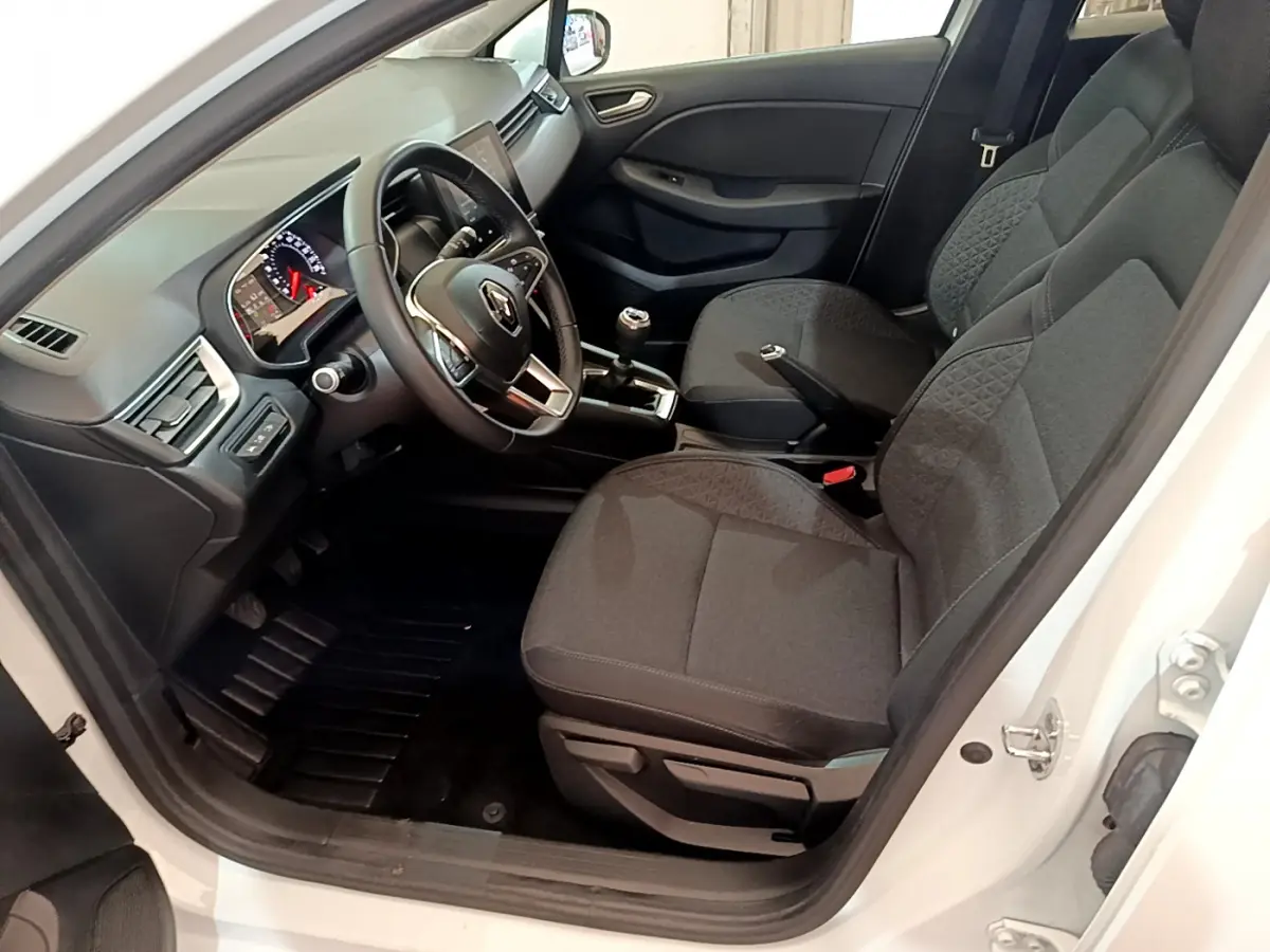 Intérieur côté conducteur de la Renault Clio Business blanche, montrant sièges noirs et tableau de bord avec écran tactile.