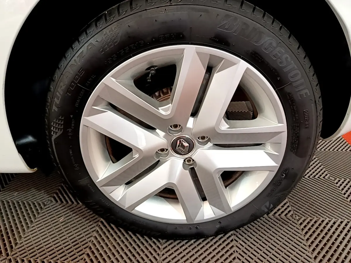 Gros plan sur la roue arrière droite blanche d'une Renault Clio Business SCe 65 de 2021, sur sol texturé.