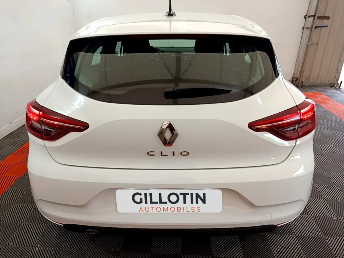 Vue arrière d'une Renault Clio blanche 2021 avec feux LED et logo Renault bien visibles sur fond intérieur showroom.