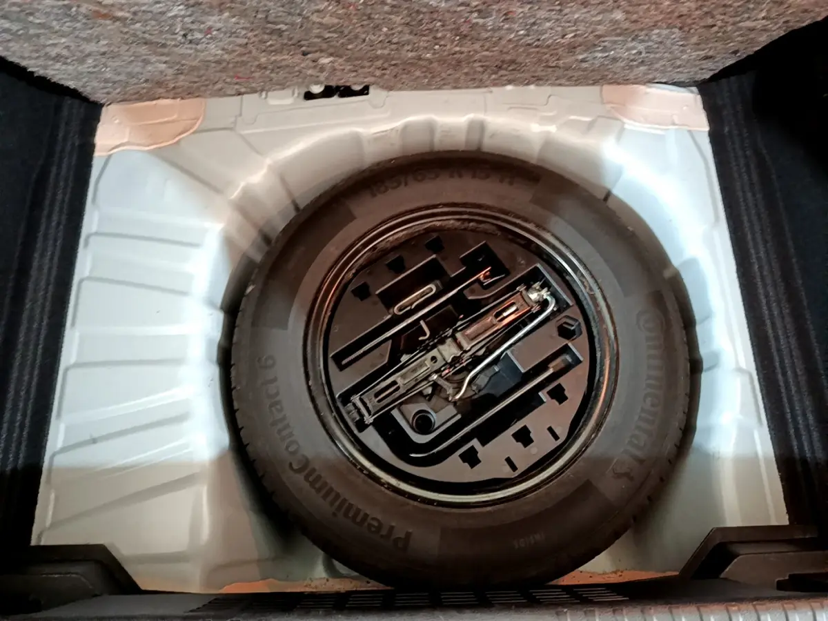 Gros plan sur la roue de secours noire et les outils de bord dans le coffre blanc d'une Renault Clio Business 2021.