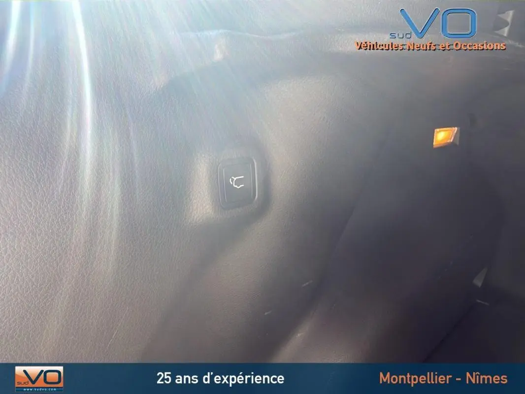 Détail intérieur du coffre du Jeep Compass gris 2023, bouton d'ouverture électrique de hayon visible sur la paroi.