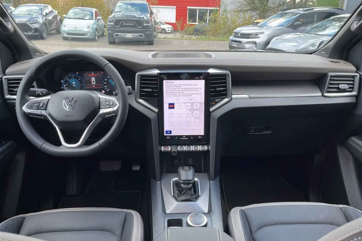 Vue intérieure du tableau de bord du Volkswagen Amarok noir, avec écran tactile vertical et volant multifonctions cuir.
