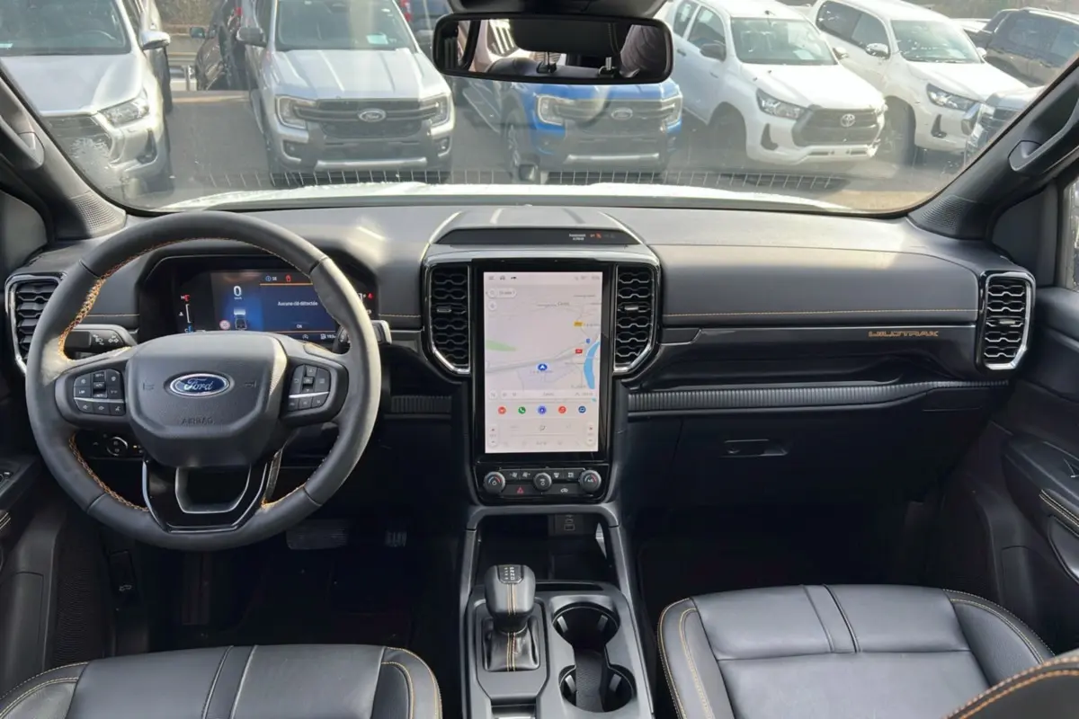 Vue intérieure avant du Ford Ranger Wildtrak 2026, tableau de bord noir avec écran tactile vertical et volant cuir noir.