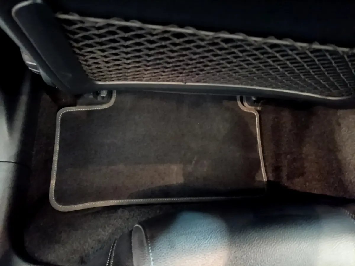 Vue intérieure du plancher arrière avec tapis de sol noir et filet de rangement sous le siège avant d'une Mercedes Classe A hybride.