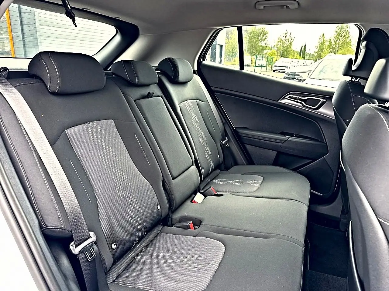 Vue latérale droite de la banquette arrière noire avec appuie-têtes et ceinture de sécurité dans un Kia Sportage 2026.