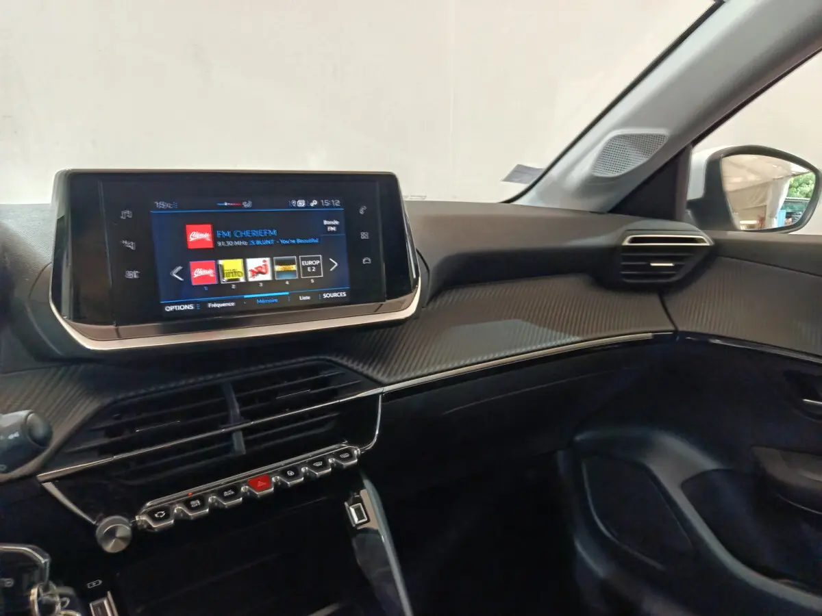 Vue intérieure côté passager du tableau de bord noir de la Peugeot 208 PureTech 100 avec écran tactile multimédia allumé.