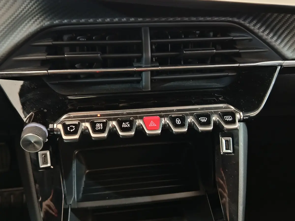 Gros plan sur la console centrale de la Peugeot 208 blanche, montrant les commandes de climatisation et les boutons fonctionnels.