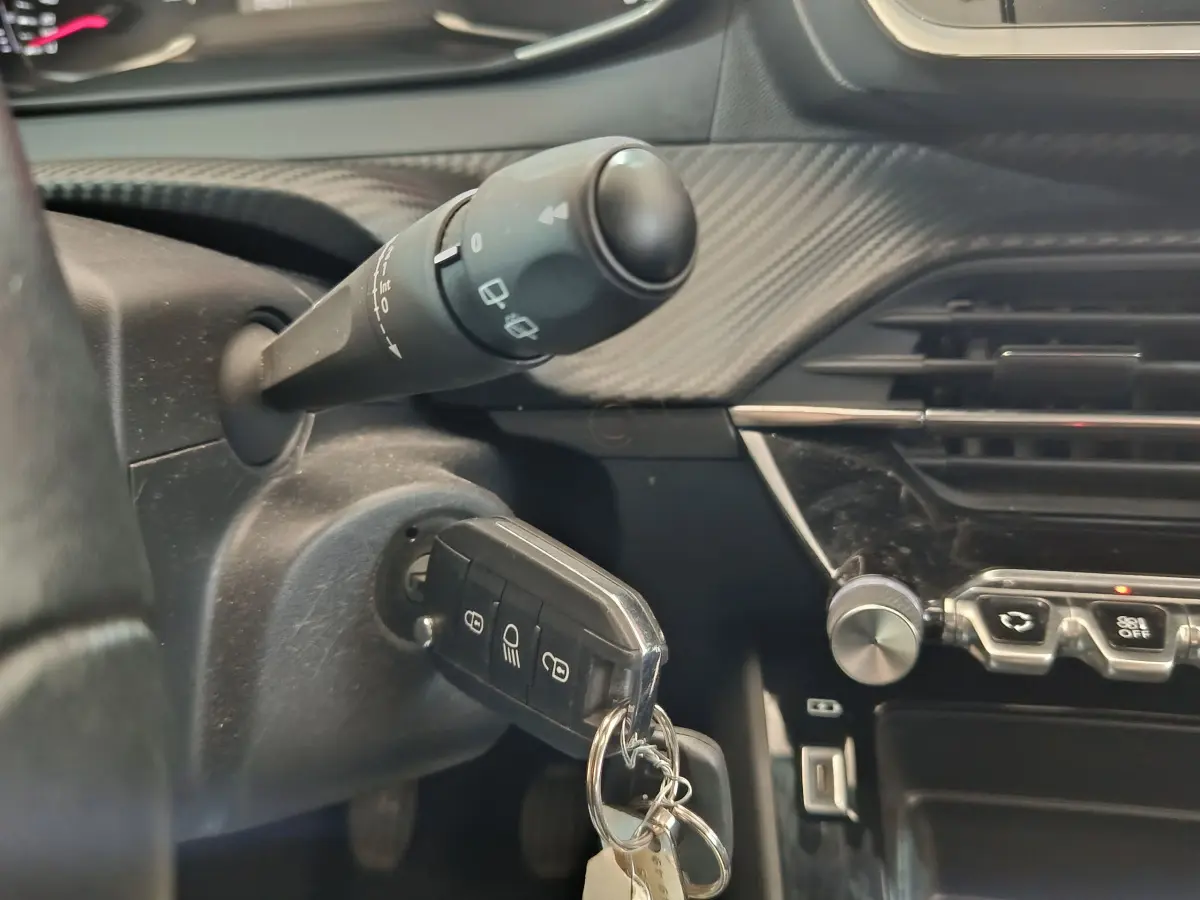 Gros plan intérieur sur le contacteur et la clé de la Peugeot 208 blanche, avec tableau de bord noir et commandes visibles.
