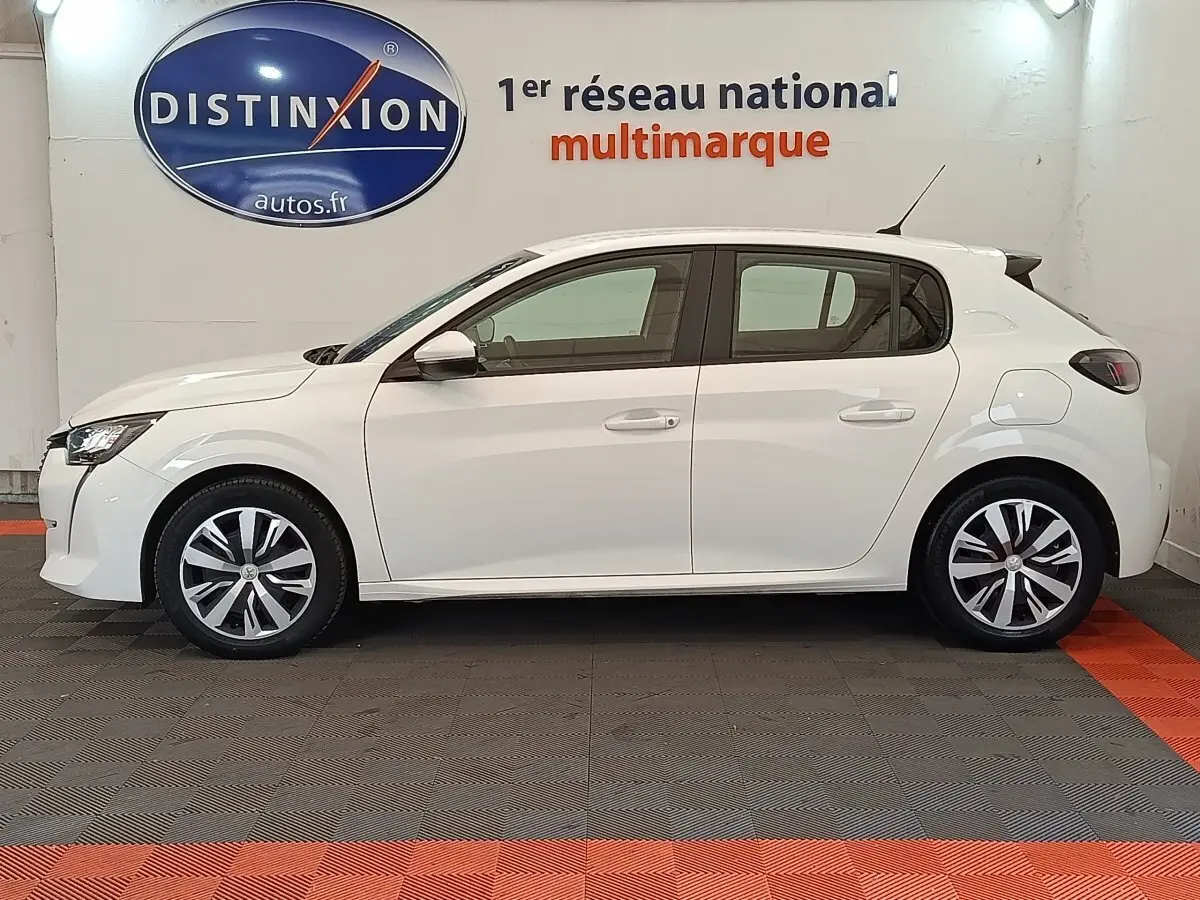Profil côté gauche d'une Peugeot 208 blanche PureTech 100 S&S Active Business de 2020 en intérieur showroom.