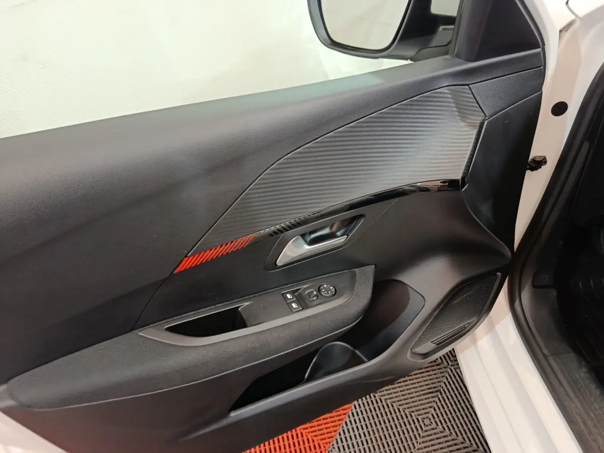 Intérieur côté conducteur de la Peugeot 208 blanche, porte avec insert carbone et bande rouge décorative.