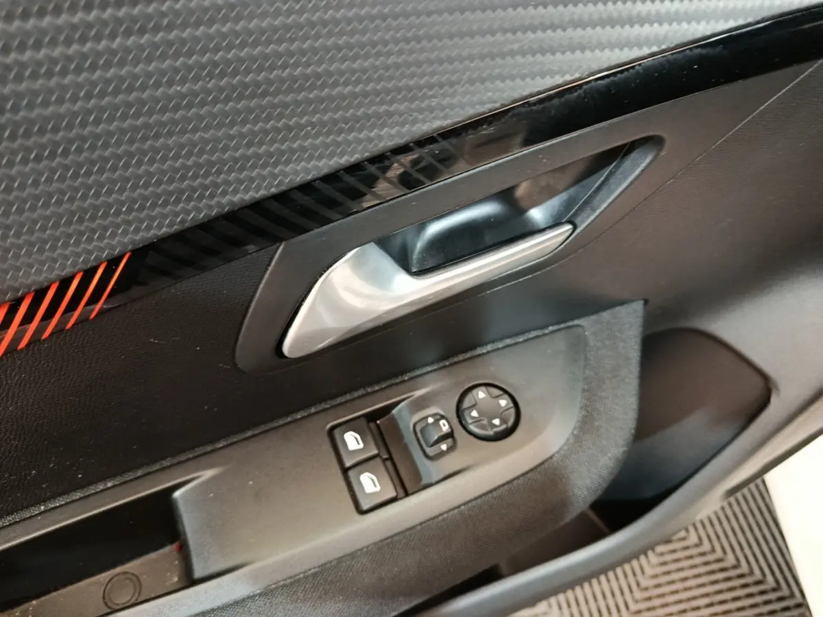 Gros plan sur la porte côté conducteur de la Peugeot 208 blanche, avec commandes électriques et poignée argentée.