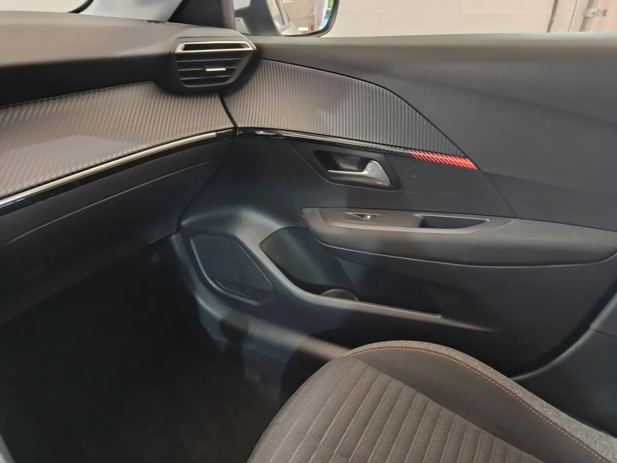 Intérieur côté passager du Peugeot 208 blanc 2020, avec garniture noire et insert décoratif rouge sur la porte.