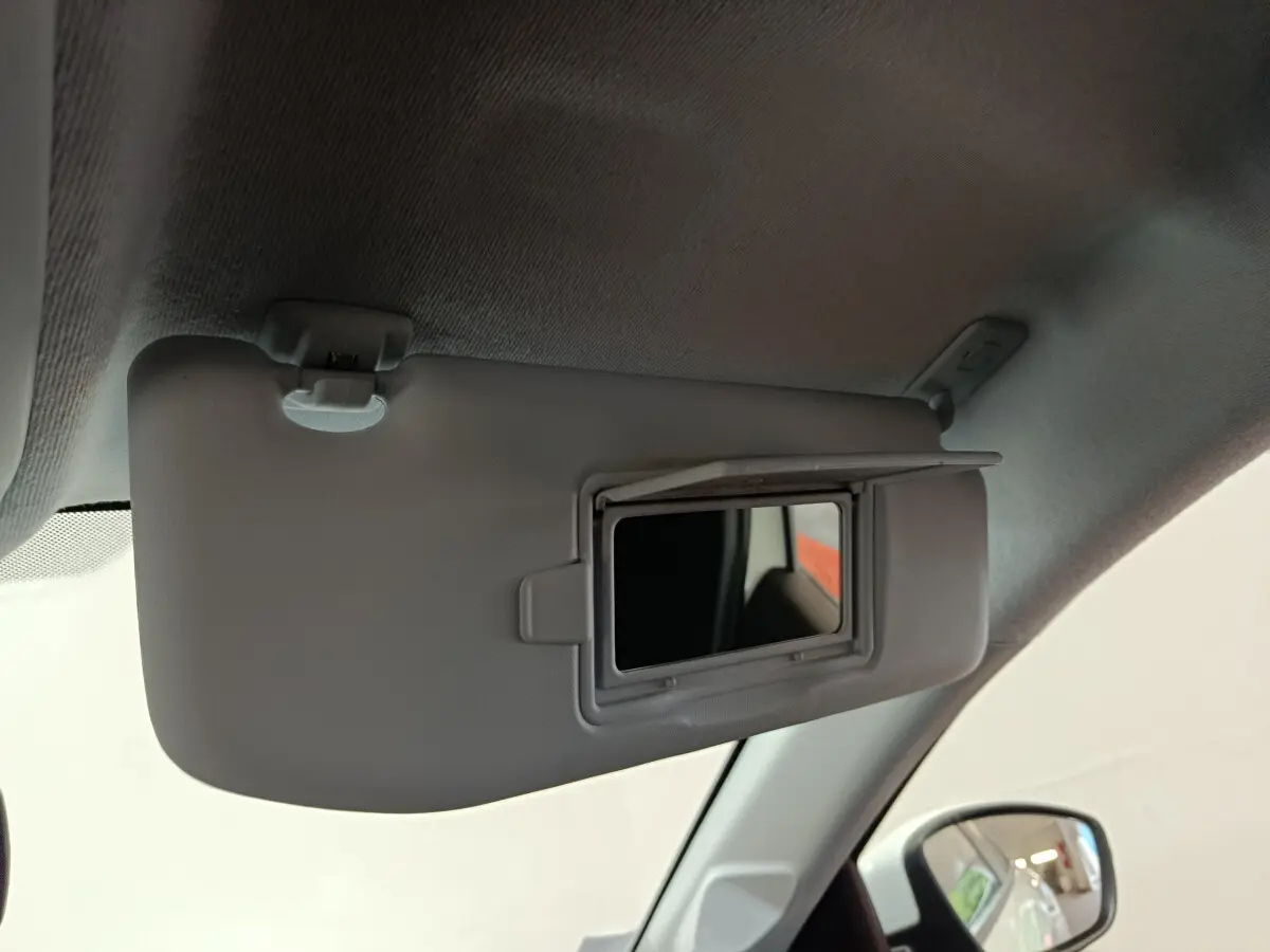 Miroir de courtoisie ouvert sur le pare-soleil côté conducteur dans l'habitacle clair d'une Peugeot 208 blanche.