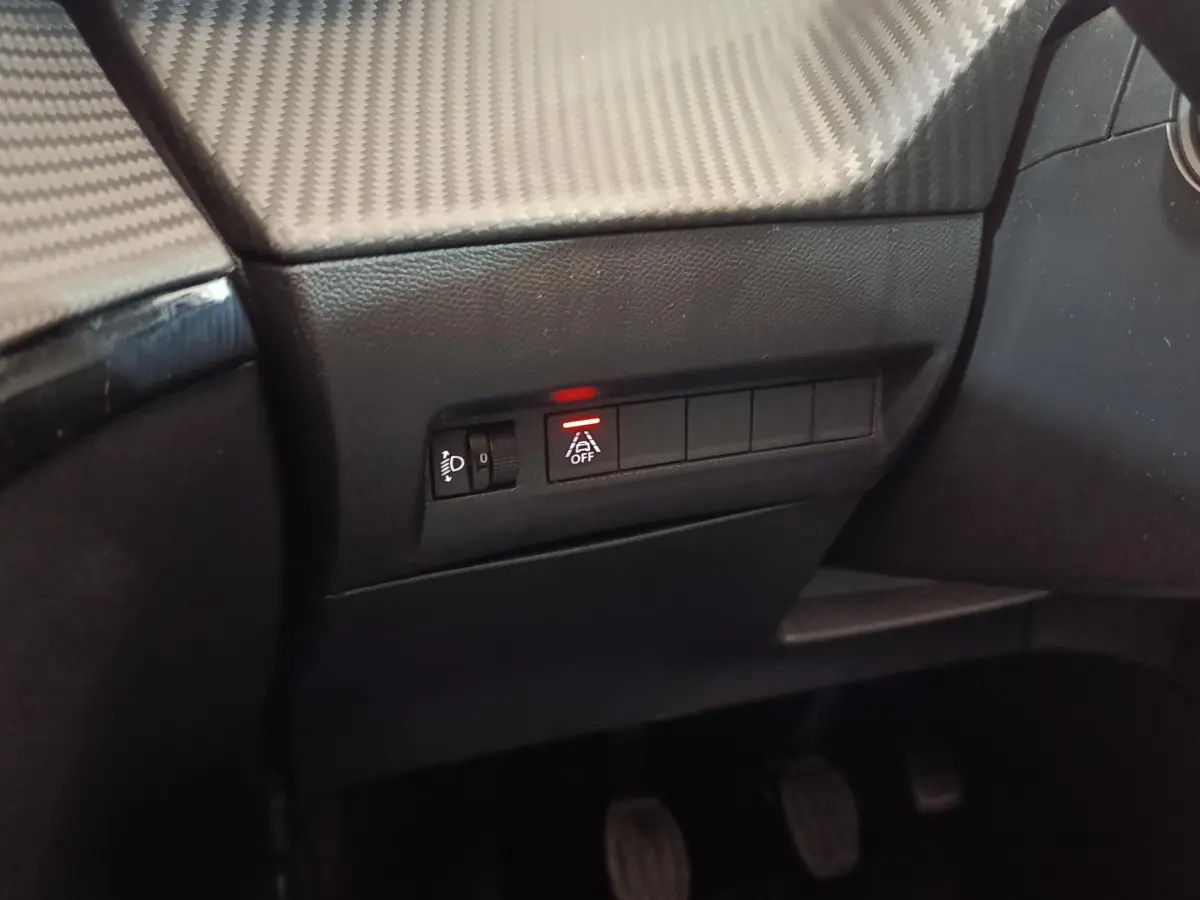 Détail du tableau de bord côté gauche d'une Peugeot 208 blanche, avec bouton d'assistance désactivée allumé en rouge.