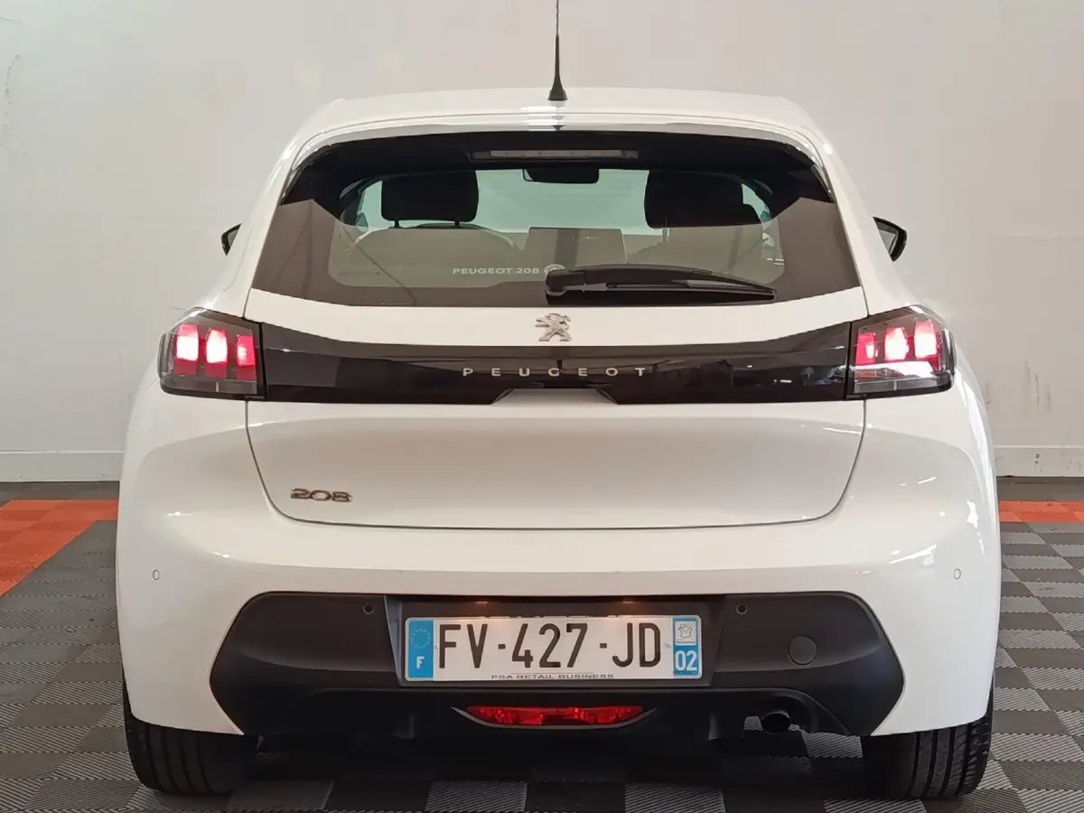 Vue arrière d'une Peugeot 208 blanche de 2020 avec feux LED allumés et bande noire distinctive sur le hayon.