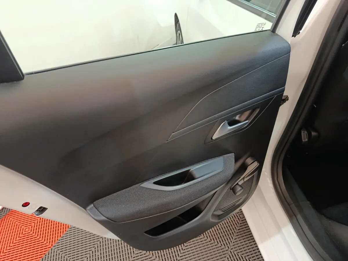 Vue rapprochée de la porte arrière droite noire intérieure d'une Peugeot 208 blanche, avec poignée et manivelle de vitre.