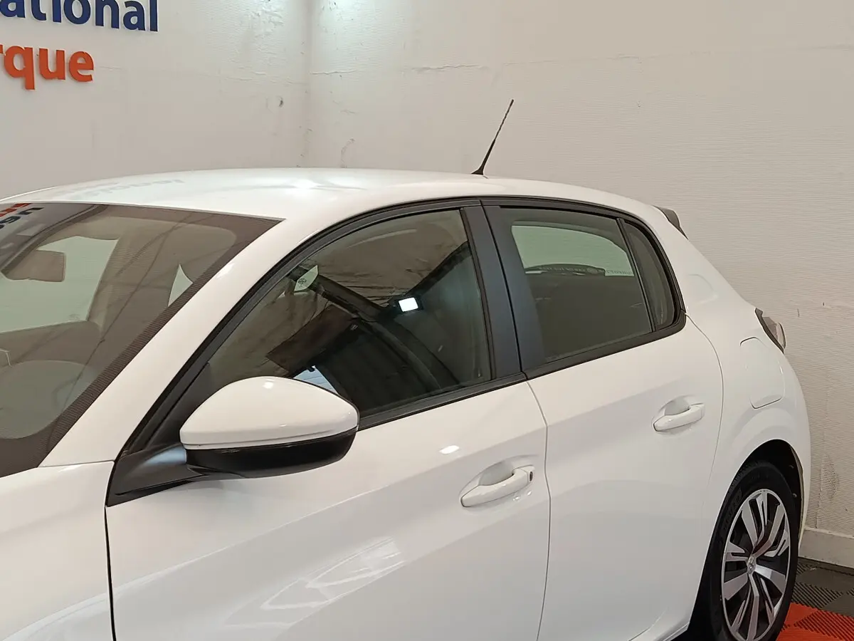 Vue latérale côté gauche d'une Peugeot 208 blanche PureTech 100 S&S Active Business, avec rétroviseur blanc et jantes stylisées.