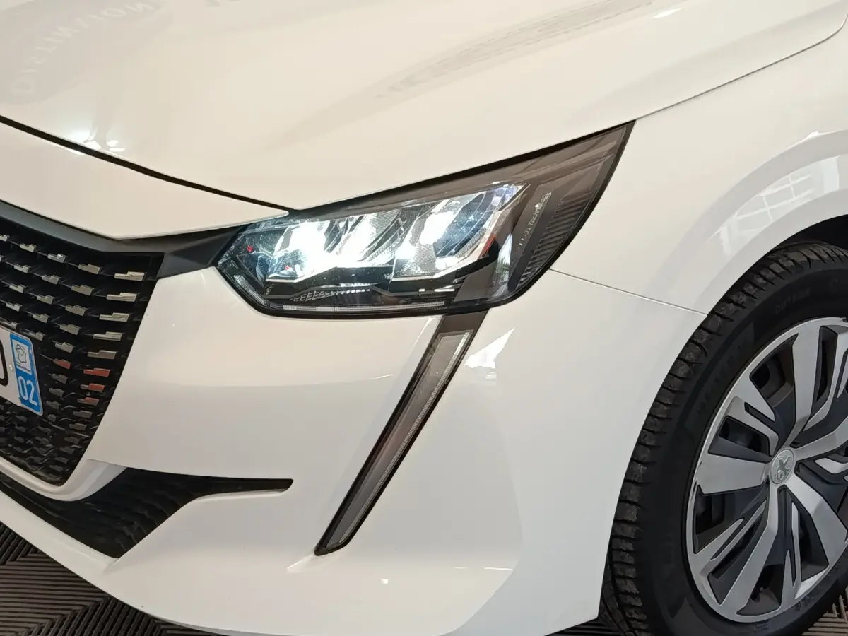 Gros plan sur l'avant droit blanc d'une Peugeot 208 2020 avec phares LED et jante alliage distinctive.