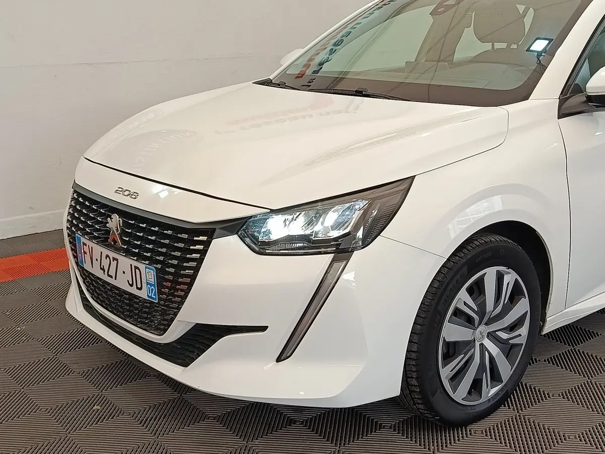 Vue 3/4 avant droit d'une Peugeot 208 blanche avec phares LED et calandre noire distinctive.