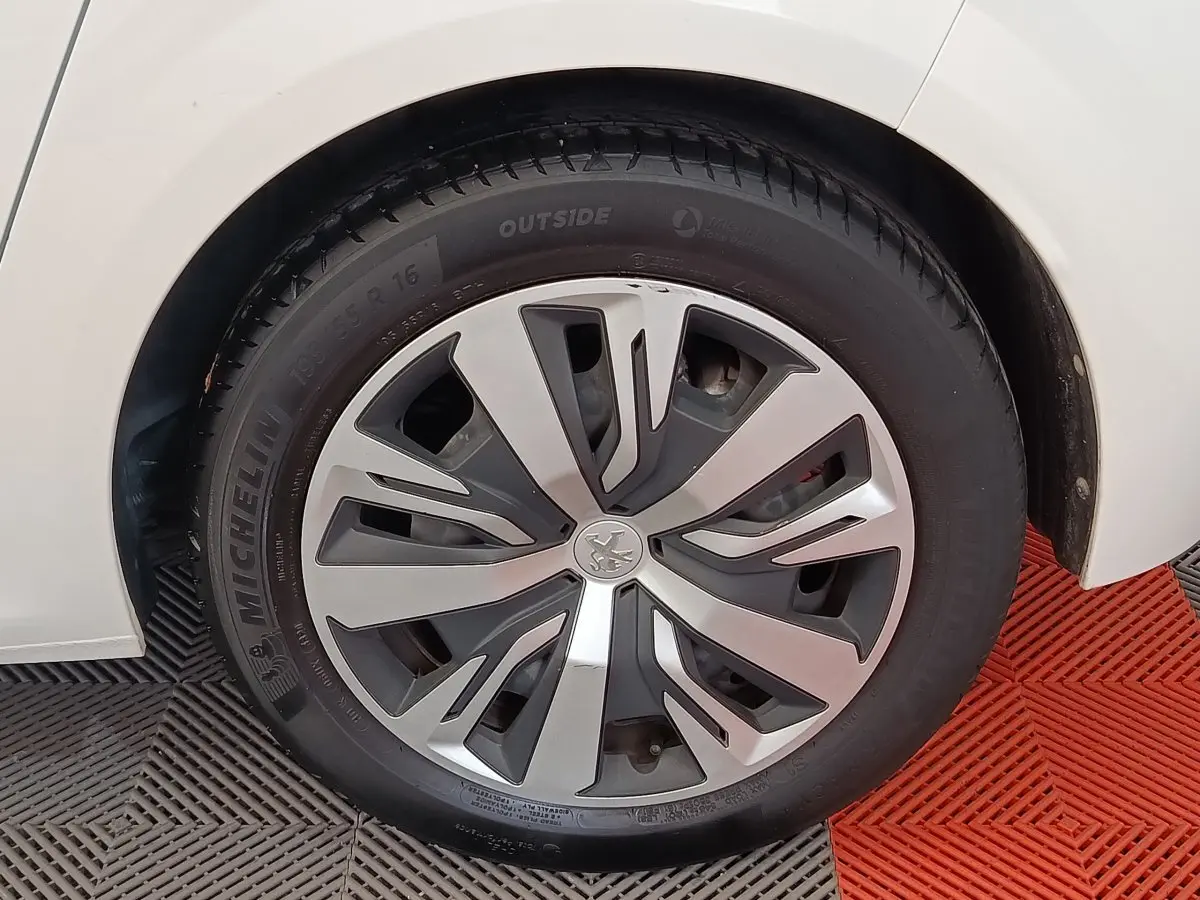 Gros plan sur la roue avant gauche d'une Peugeot 208 blanche, avec jante alliage au design moderne.