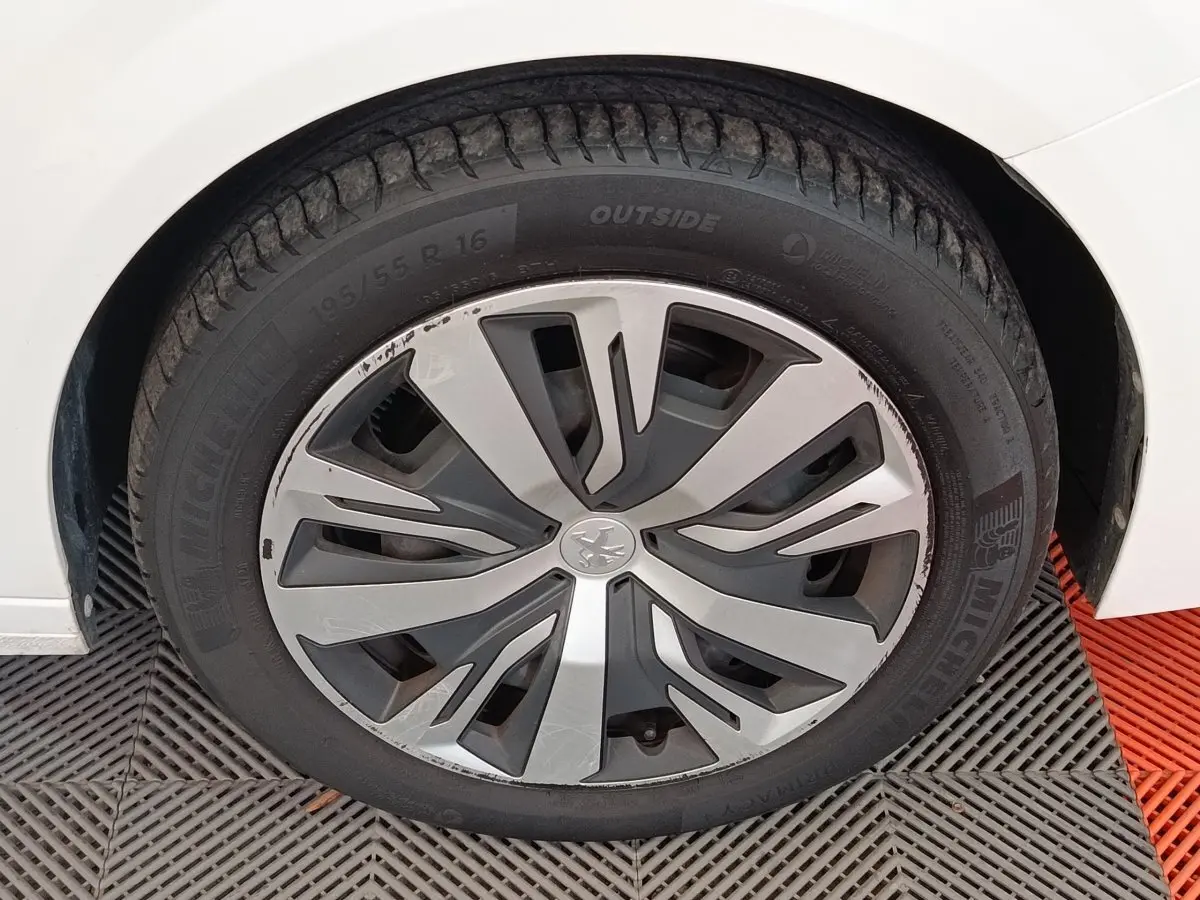 Gros plan sur la roue avant gauche d'une Peugeot 208 blanche, avec jante alliage au design moderne.