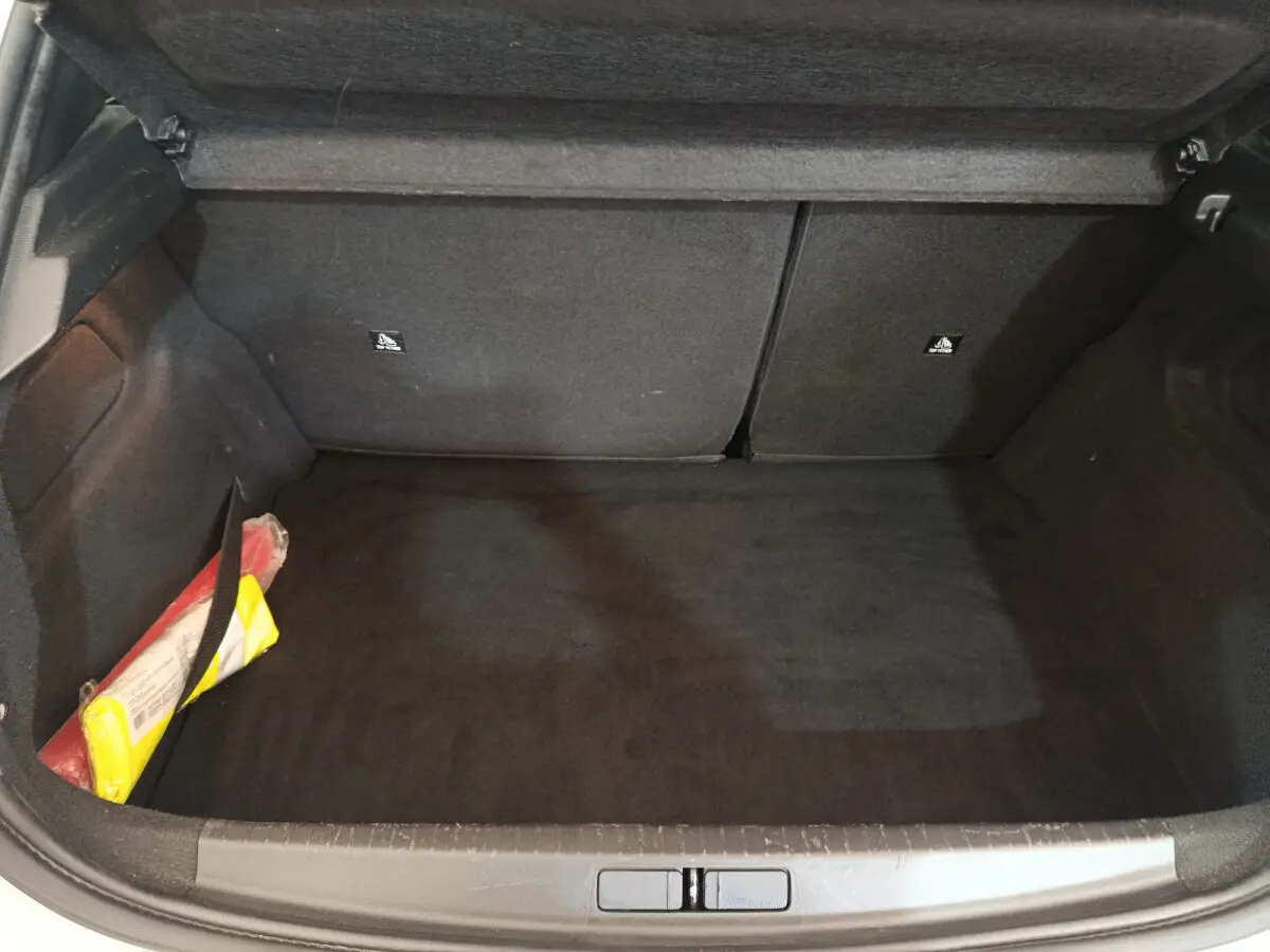 Coffre ouvert d'une Peugeot 208 blanche, vue de dessus, montrant un espace de chargement vide avec un kit de sécurité sur le côté.