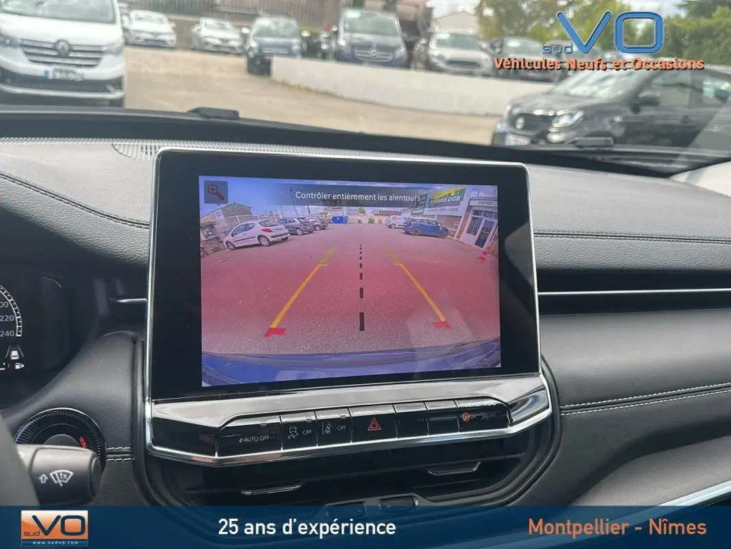 Vue intérieure du tableau de bord du Jeep Compass bleu 2023 avec écran tactile affichant la caméra de recul et aides au stationnement.