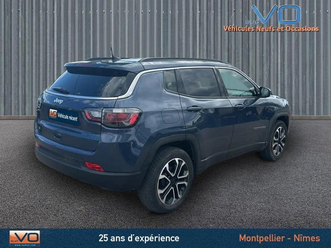 Jeep Compass bleu vue 3/4 arrière droit, avec barres de toit et jantes 18 pouces visibles sur sol goudronné.