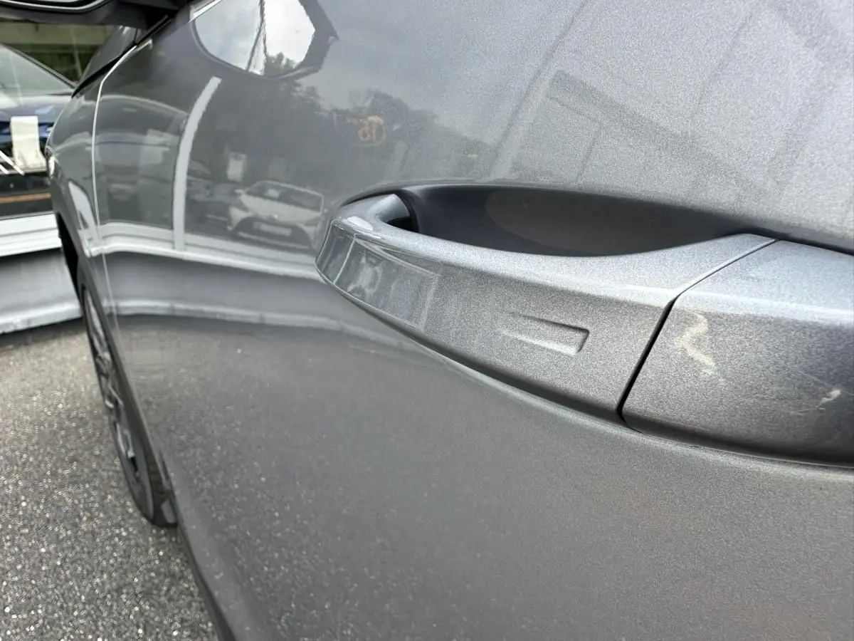 Gros plan sur la poignée de porte côté gauche du Peugeot 3008 gris Artense, reflétant l'environnement extérieur.