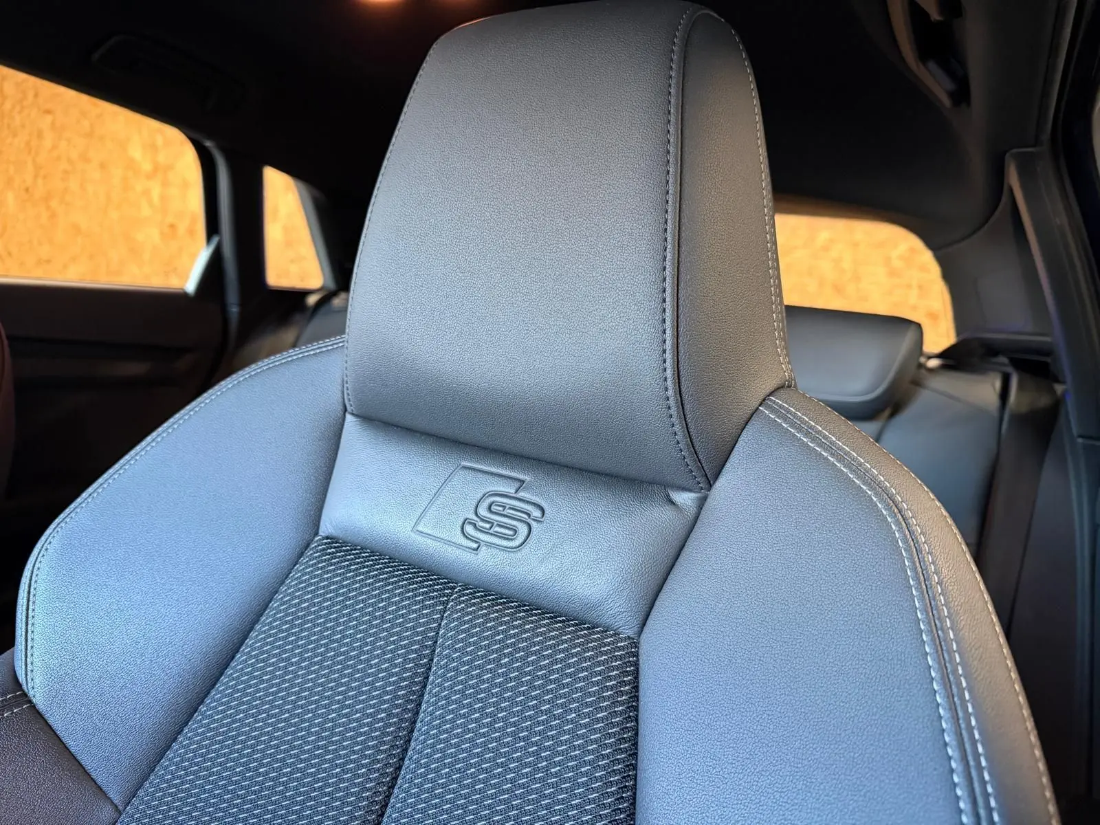 Gros plan sur le siège avant en cuir noir de l'Audi A3 S-Line avec logo "S" embossé, intérieur visible en arrière-plan.