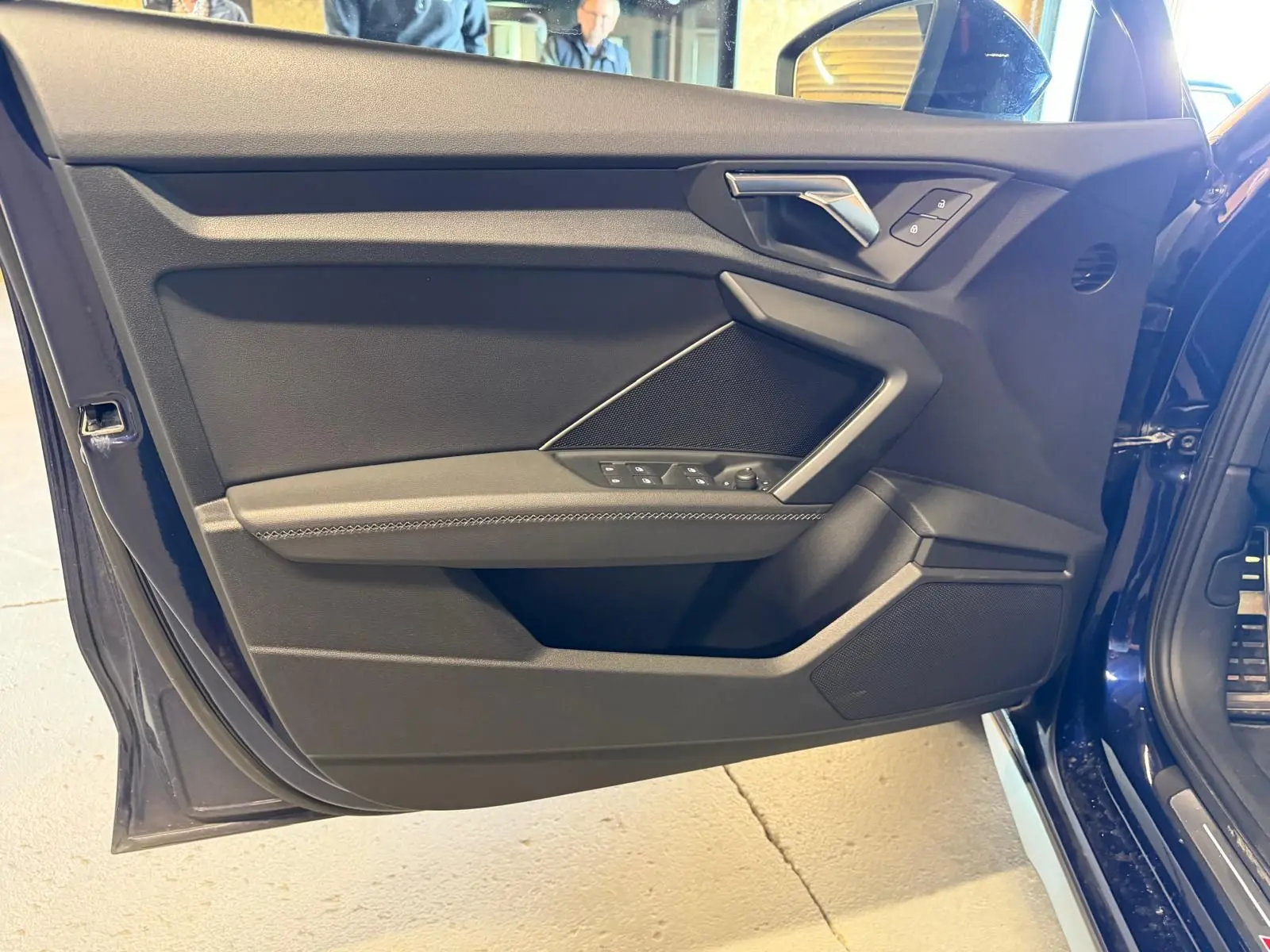 Vue rapprochée de la porte avant gauche bleu foncé d’une Audi A3 2.0 TDI S-Line avec commandes de vitres et poignée argentée.