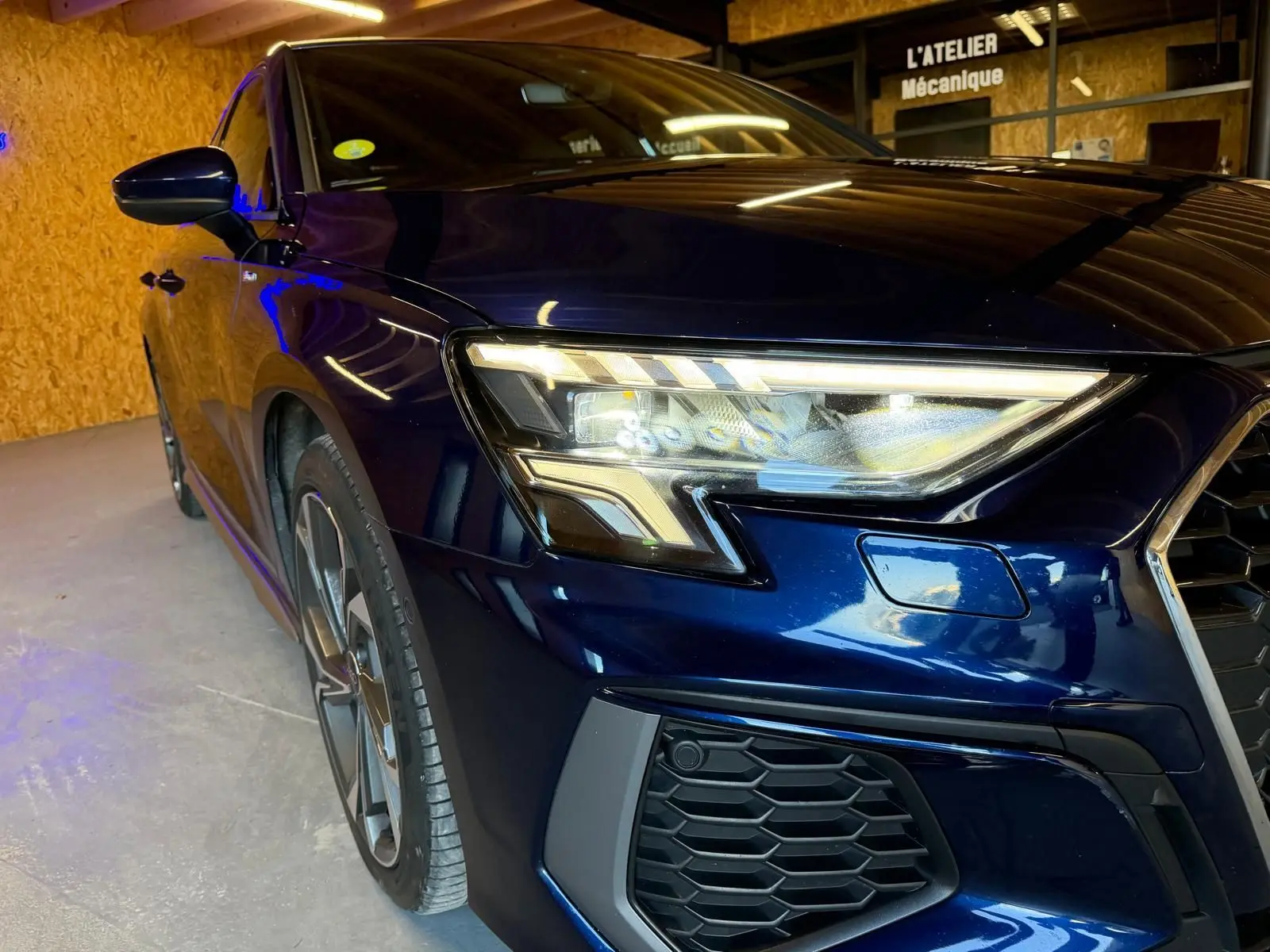 Vue 3/4 avant gauche d'une Audi A3 2.0 TDI S-Line bleu foncé avec phares LED et calandre hexagonale.