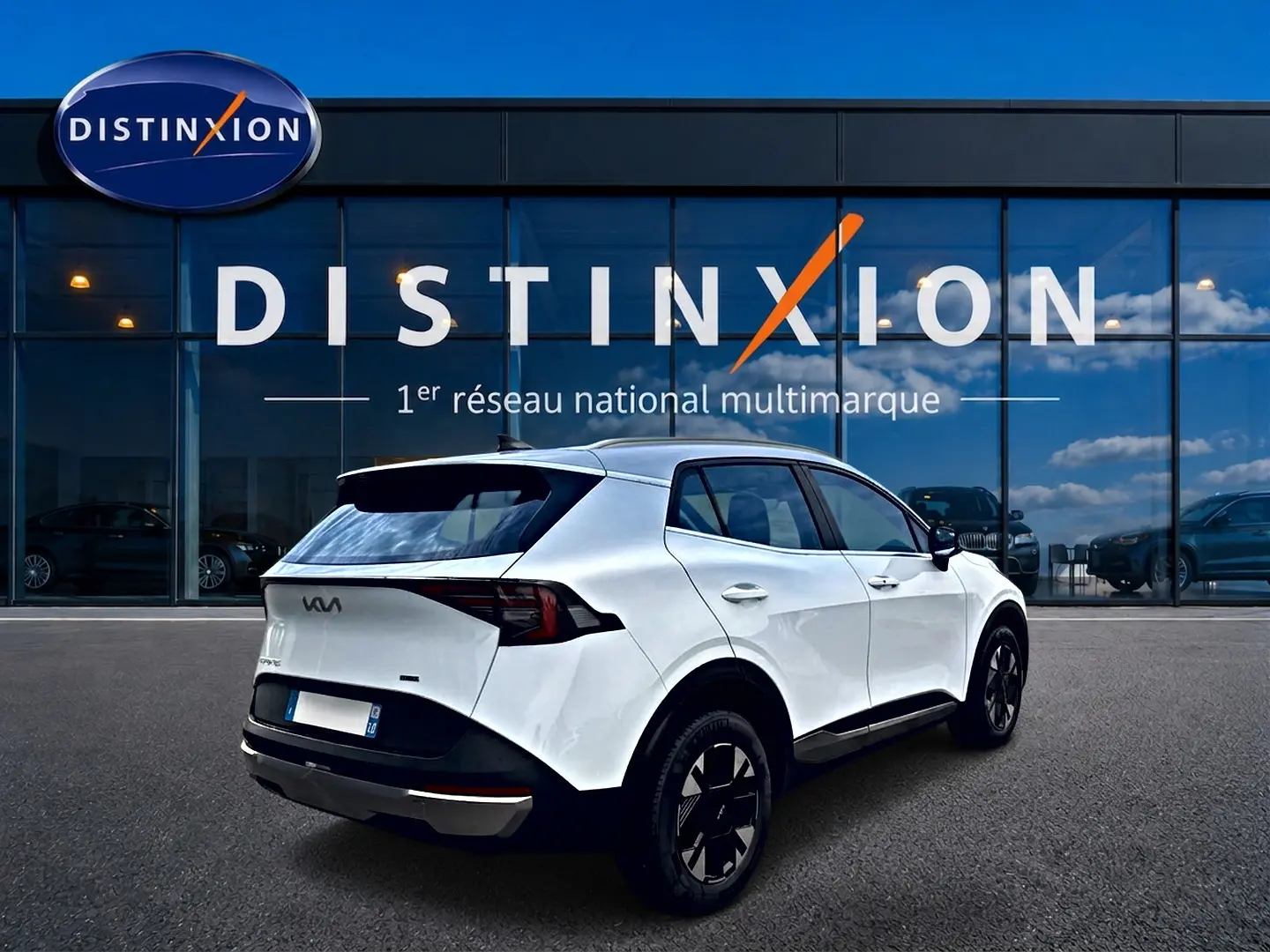 Vue 3/4 arrière droite d'un KIA Sportage blanc 2026 devant une vitrine avec logo Distinxion.